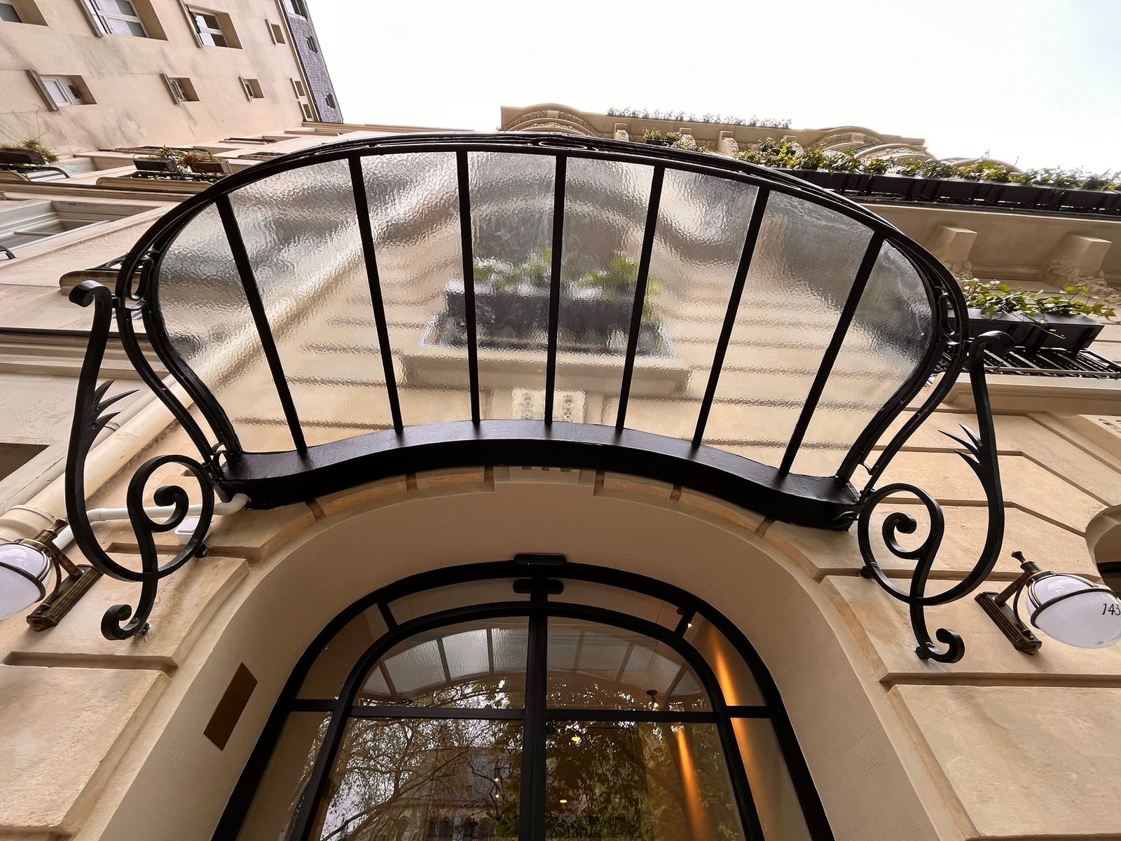 Marquise cintrée en fer forgé et verre, vue de dessous, au-dessus d’une porte cochère.