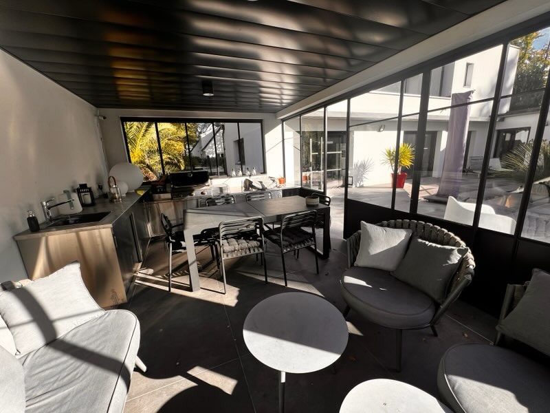 Salle de réception vitrée sous une ossature d’acier noir, ouverte sur une cour.